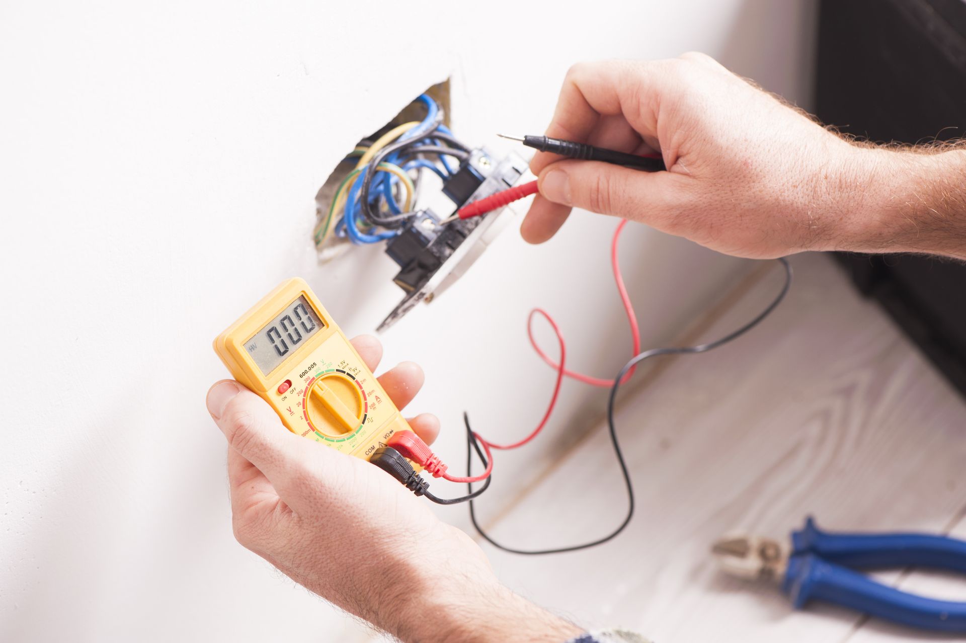 Electrician testing electrical outlet with a multimeter, tools nearby.