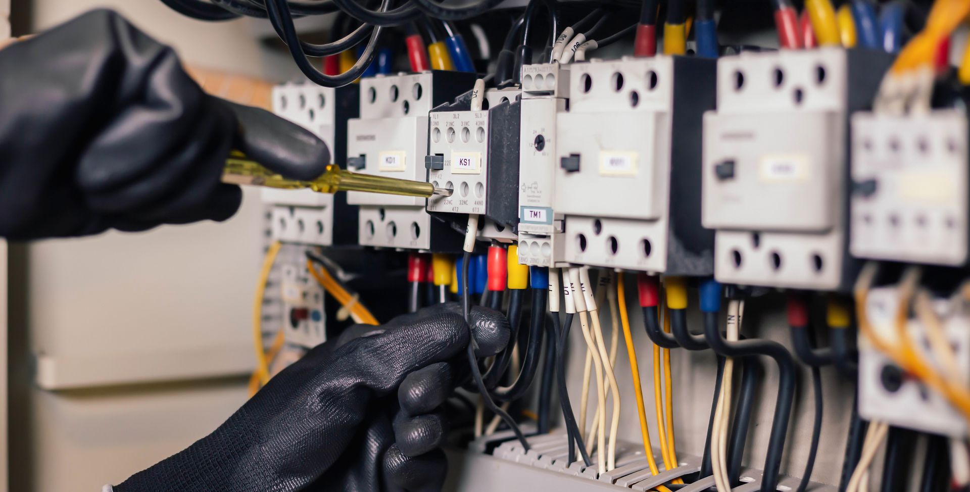 Hands in black gloves working on electrical wiring in a panel. Wires are multi-colored.