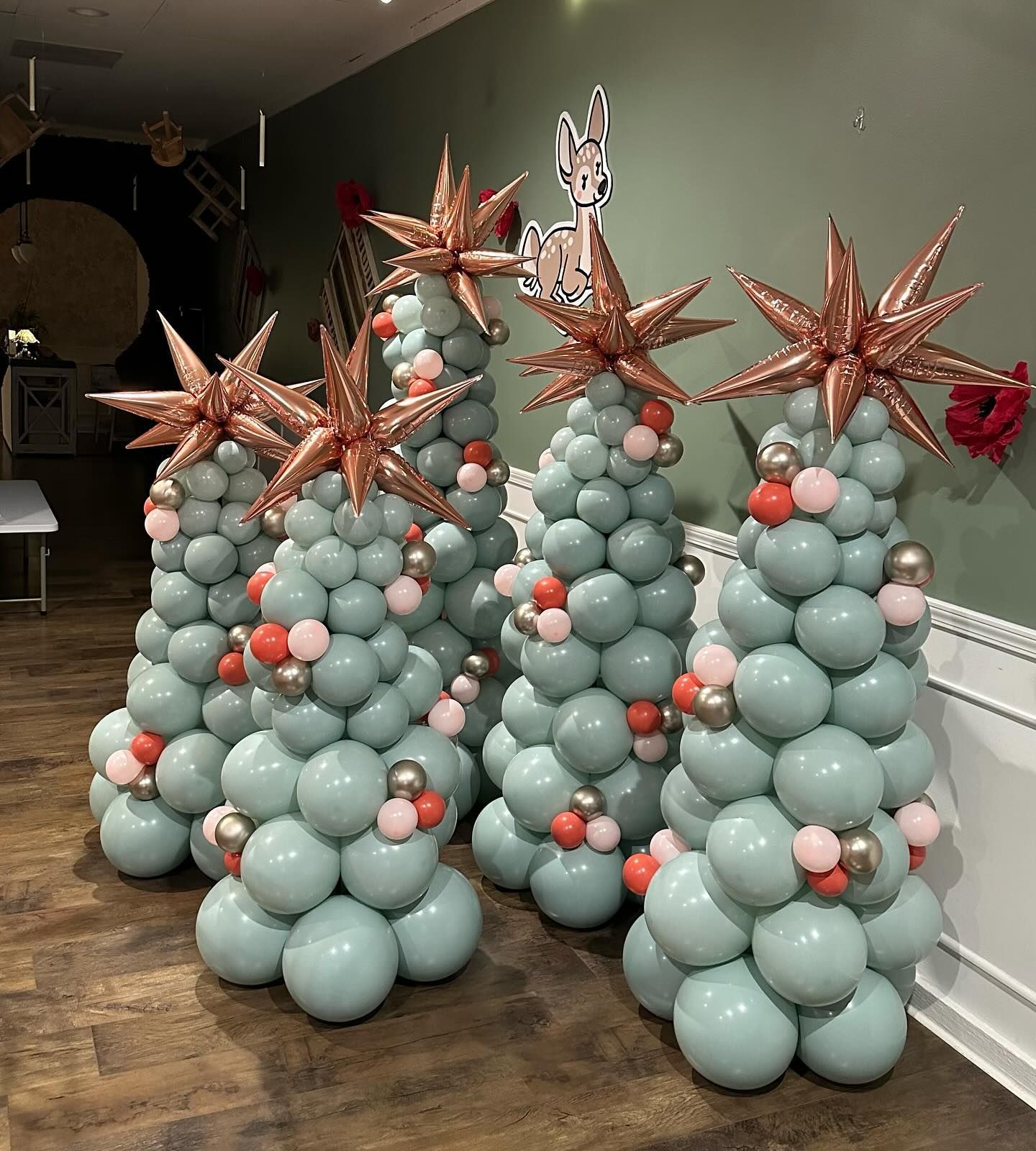 Three balloon christmas trees are sitting on a wooden floor in a room.