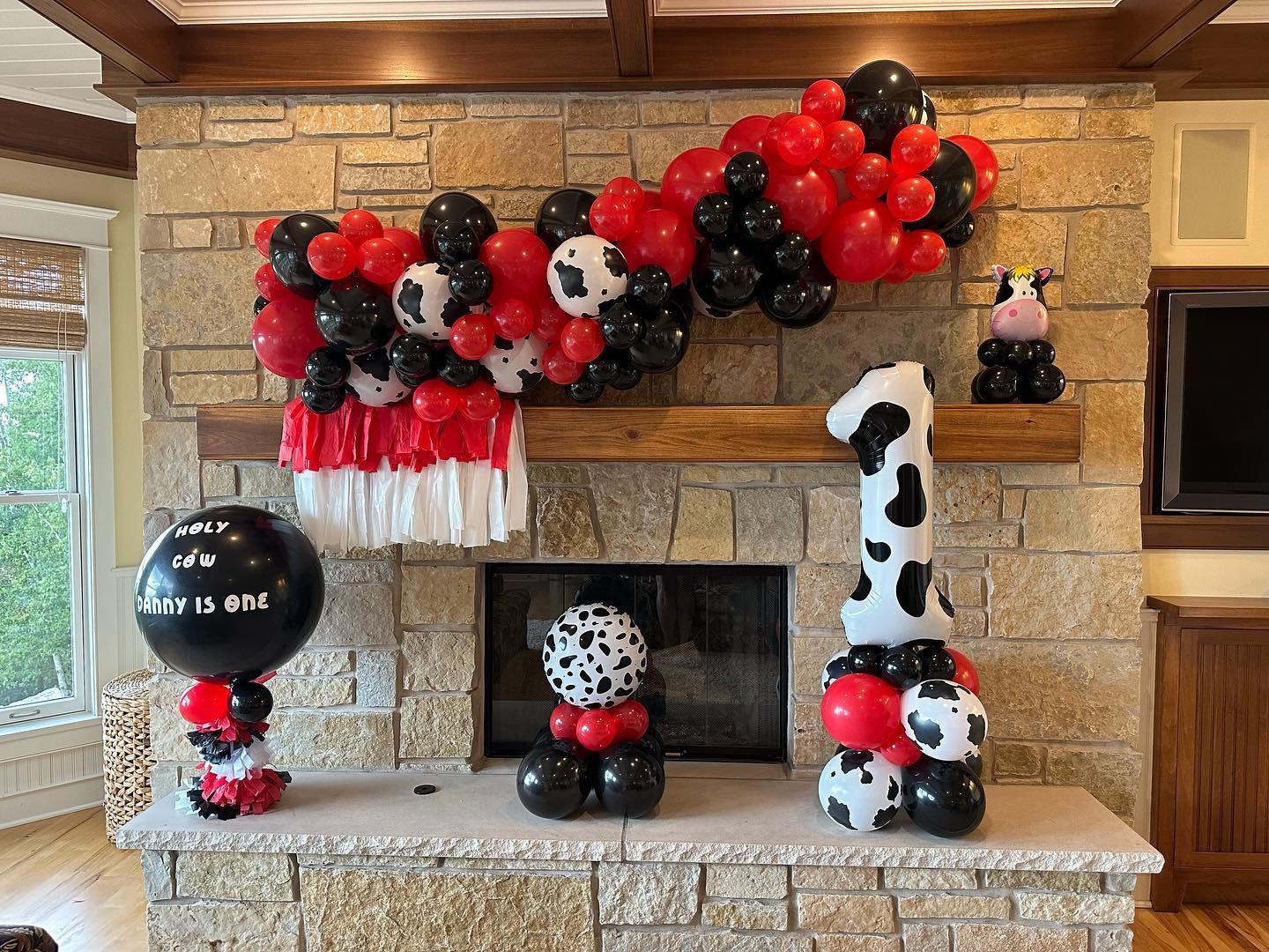 A fireplace decorated with red , black and white balloons and a cow.