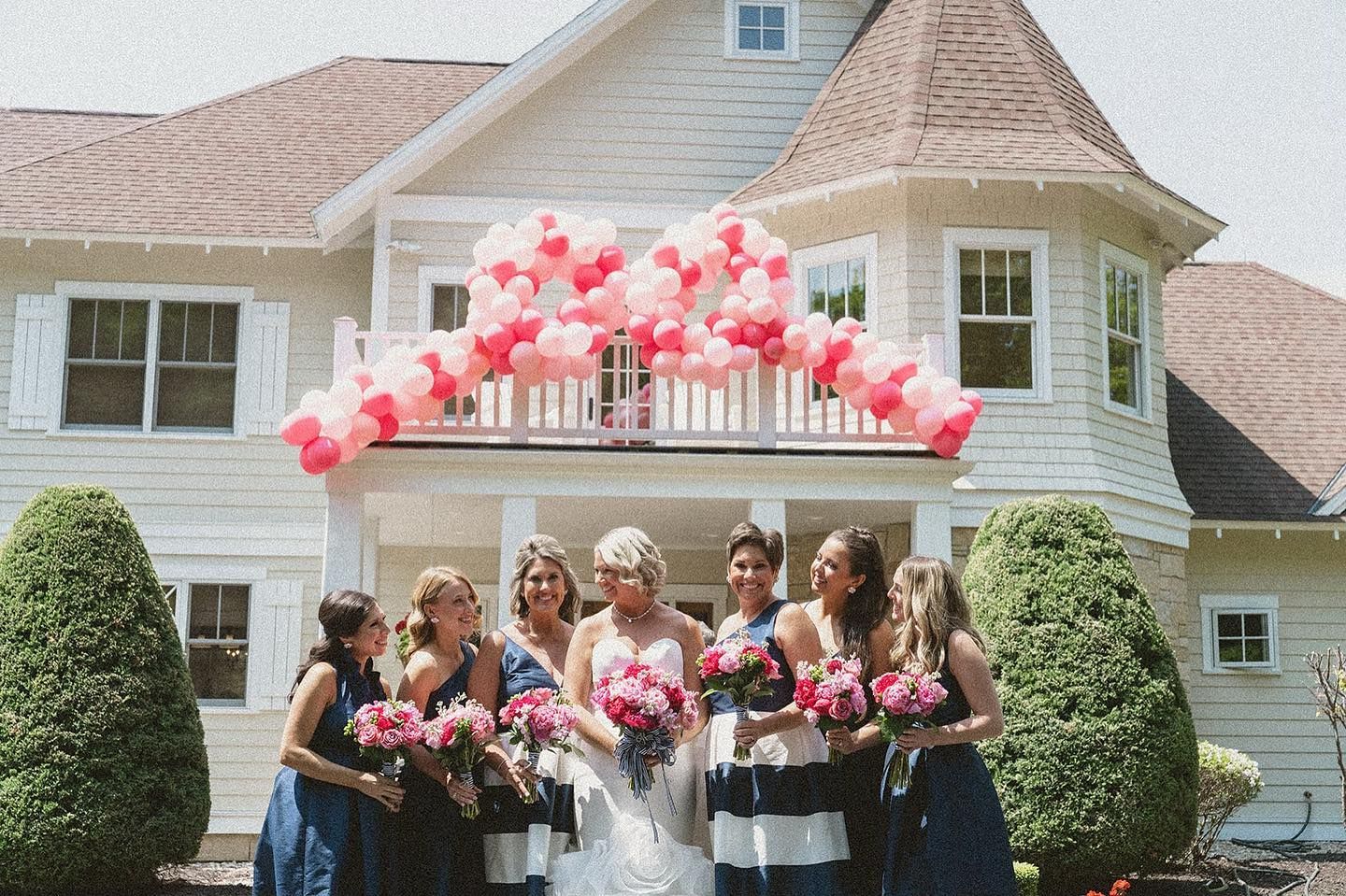 A bride and her bridesmaids are posing for a picture in front of a house.