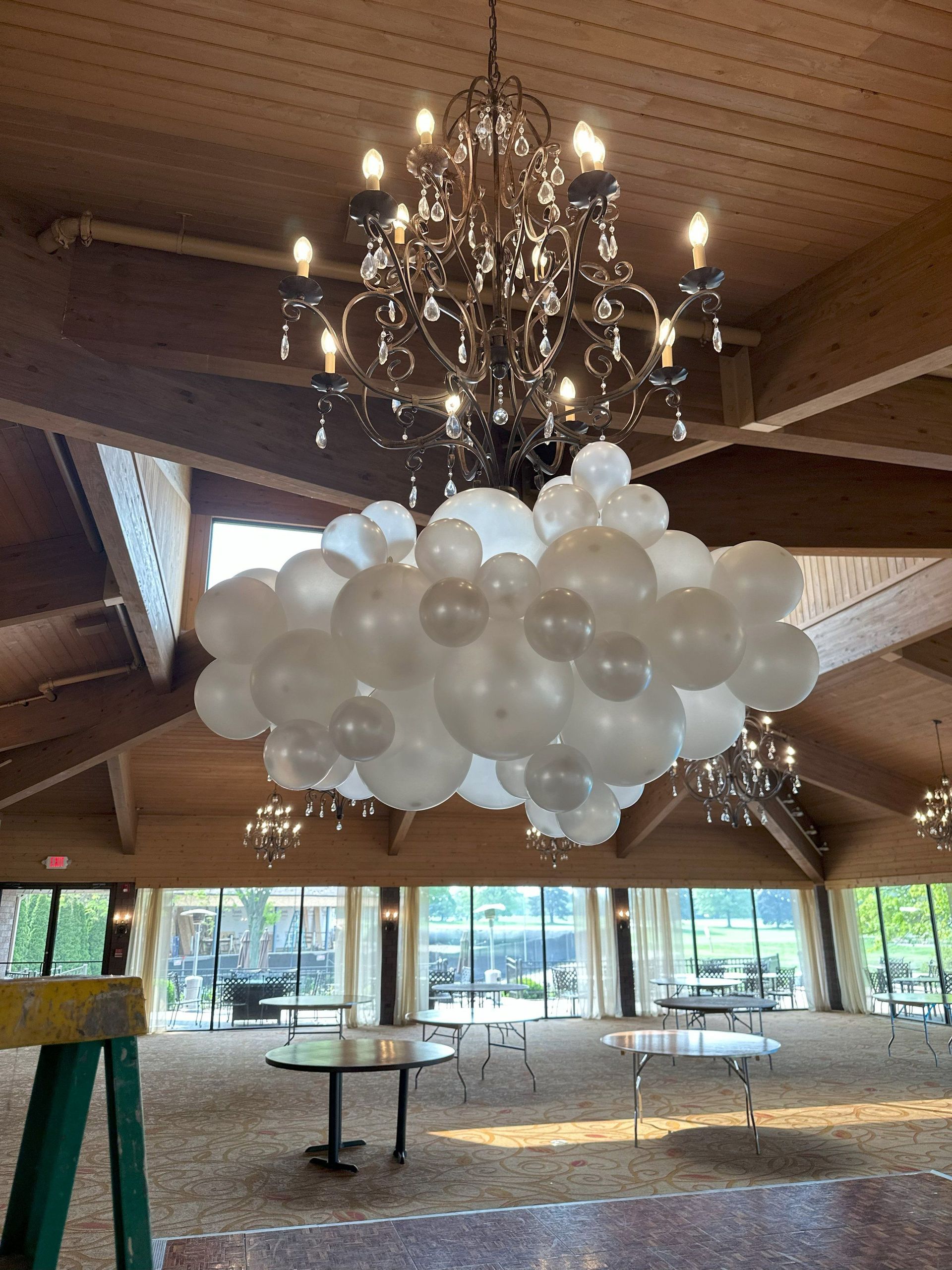 A bunch of white balloons are hanging from a chandelier in a room.