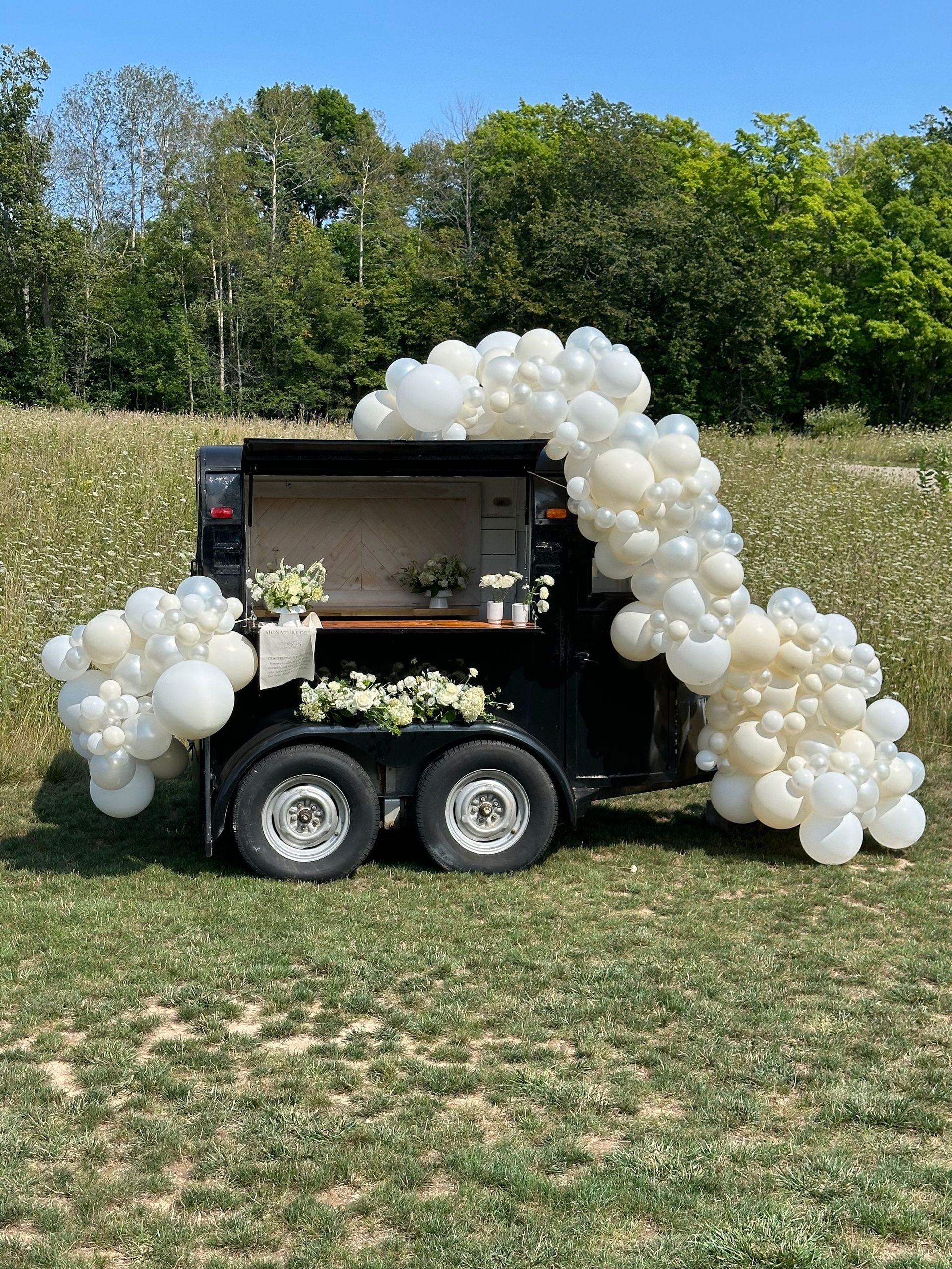 A trailer is decorated with white balloons in a field.