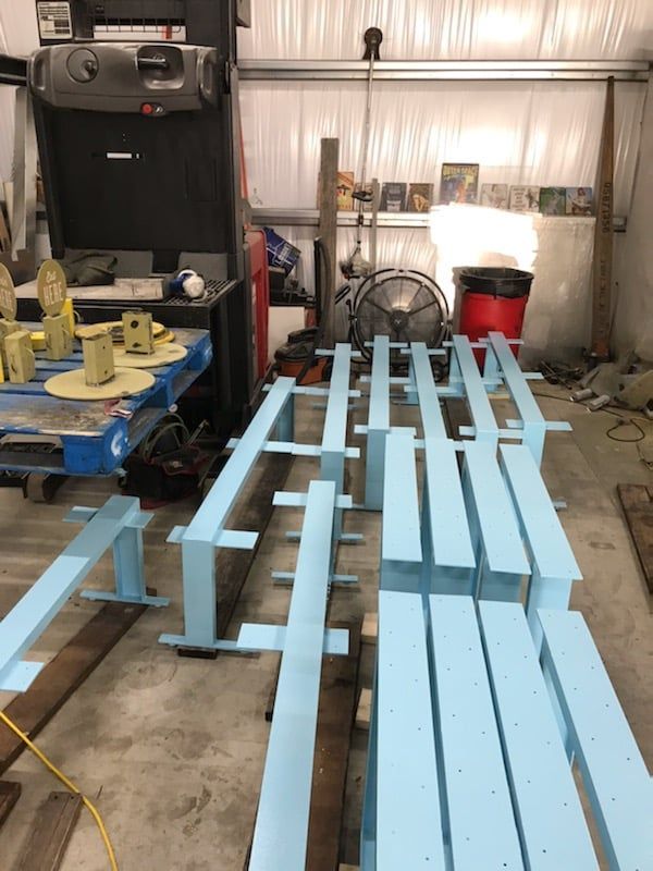 Blue painted lumber stacked in a garage; wheel balancer and fan visible in the background.