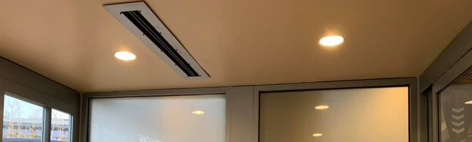 Ceiling with recessed lighting and air vent above glass windows.