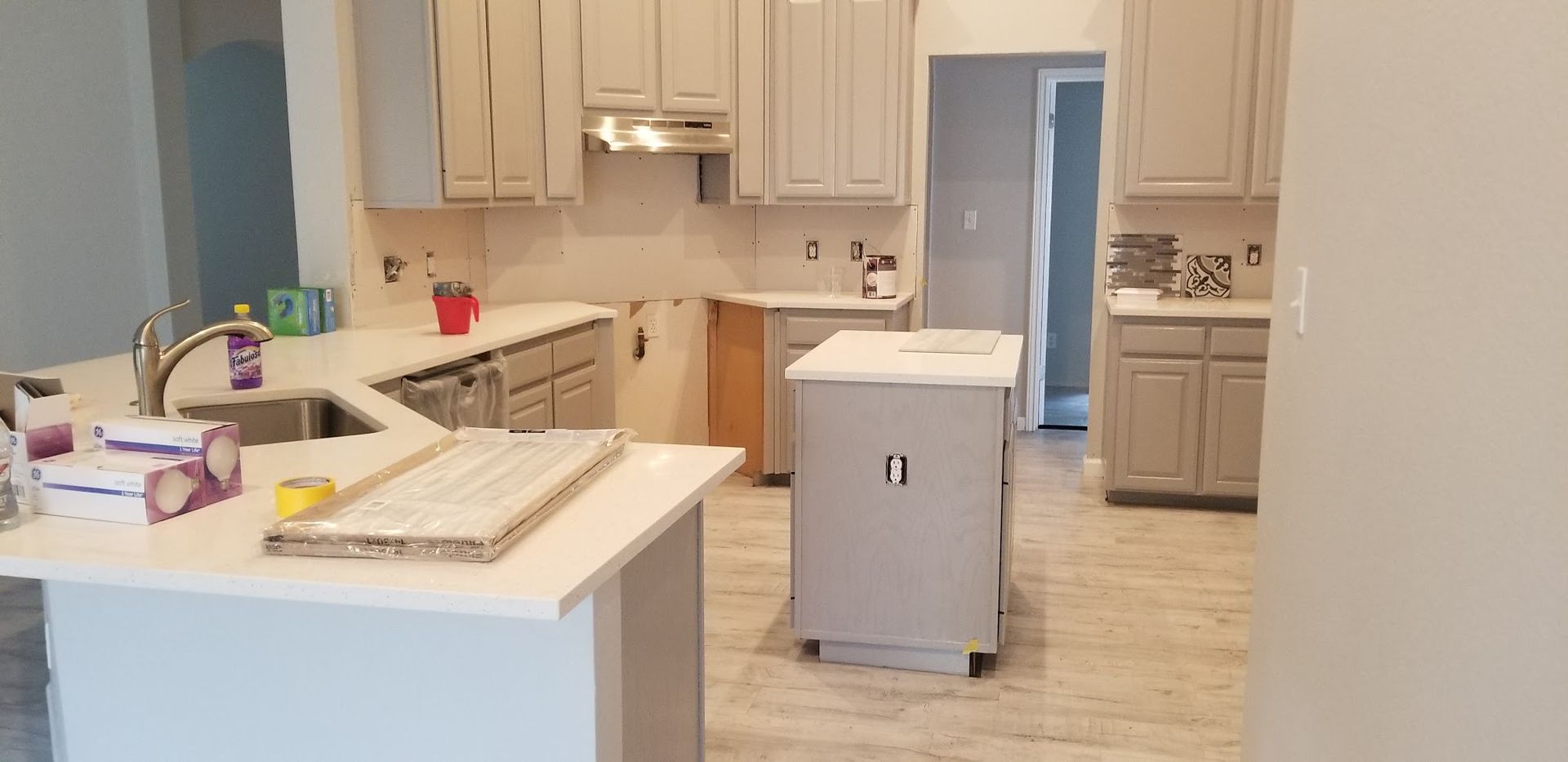 Kitchen with light gray cabinets, white countertops, and a gray island, showing renovation work in progress.
