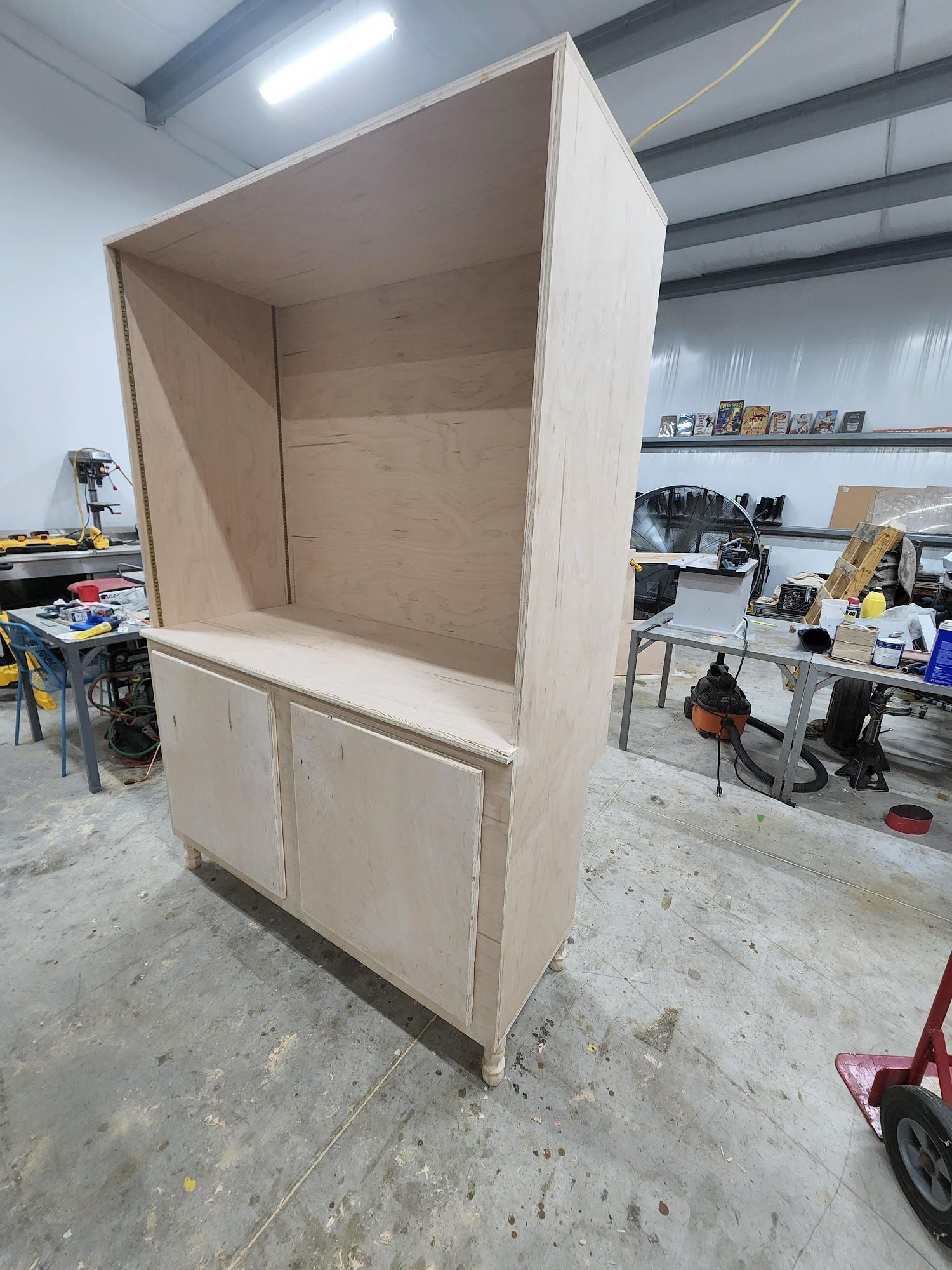 A tall unfinished wooden cabinet with two lower doors, in a workshop setting.