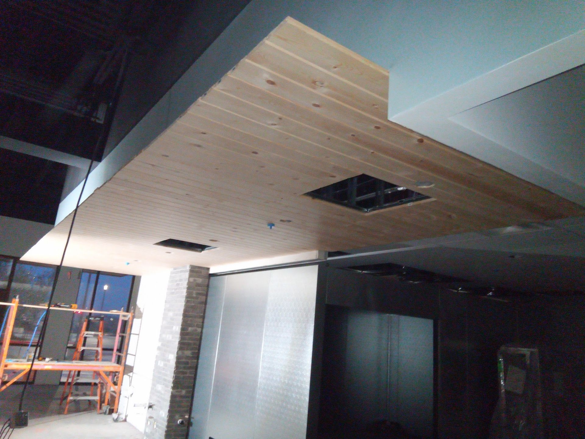 Wooden ceiling construction with recessed lighting and a dark gray wall. Construction setting.