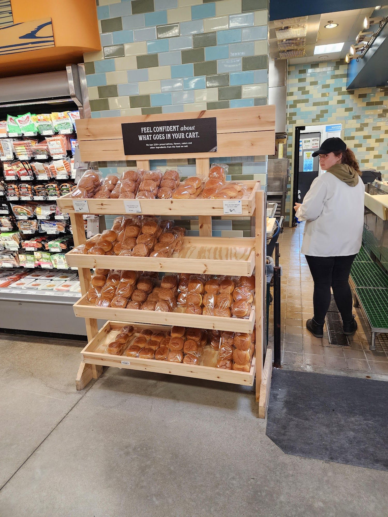 Wooden bakery display with packaged pastries inside a store, a person standing nearby.