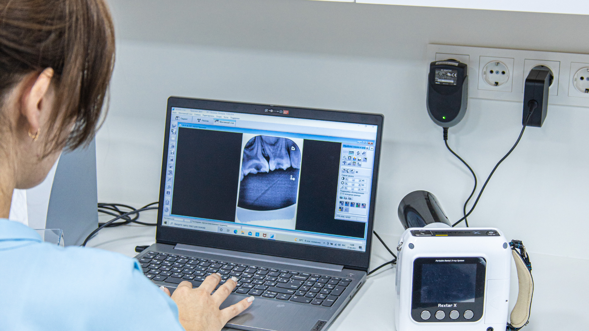 Woman examining x-ray on laptop, connected to a portable x-ray machine in a medical setting.