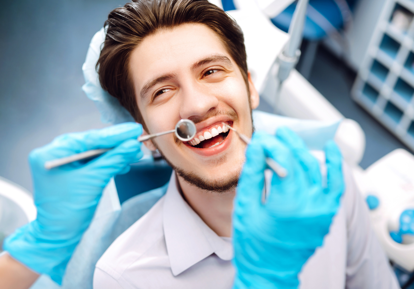 Man smiling during dental exam; dentist using tools in blue-gloved hands.