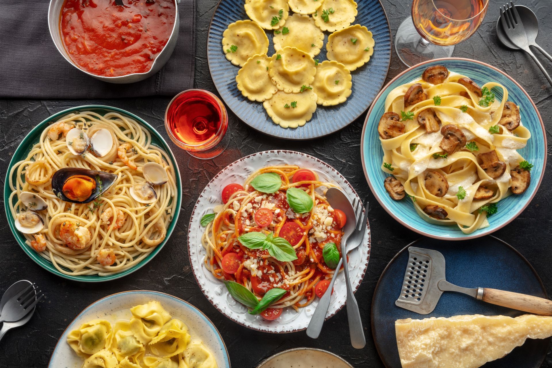 An overhead flat lay shot on a black background of pasta variety, Italian food, and drinks.