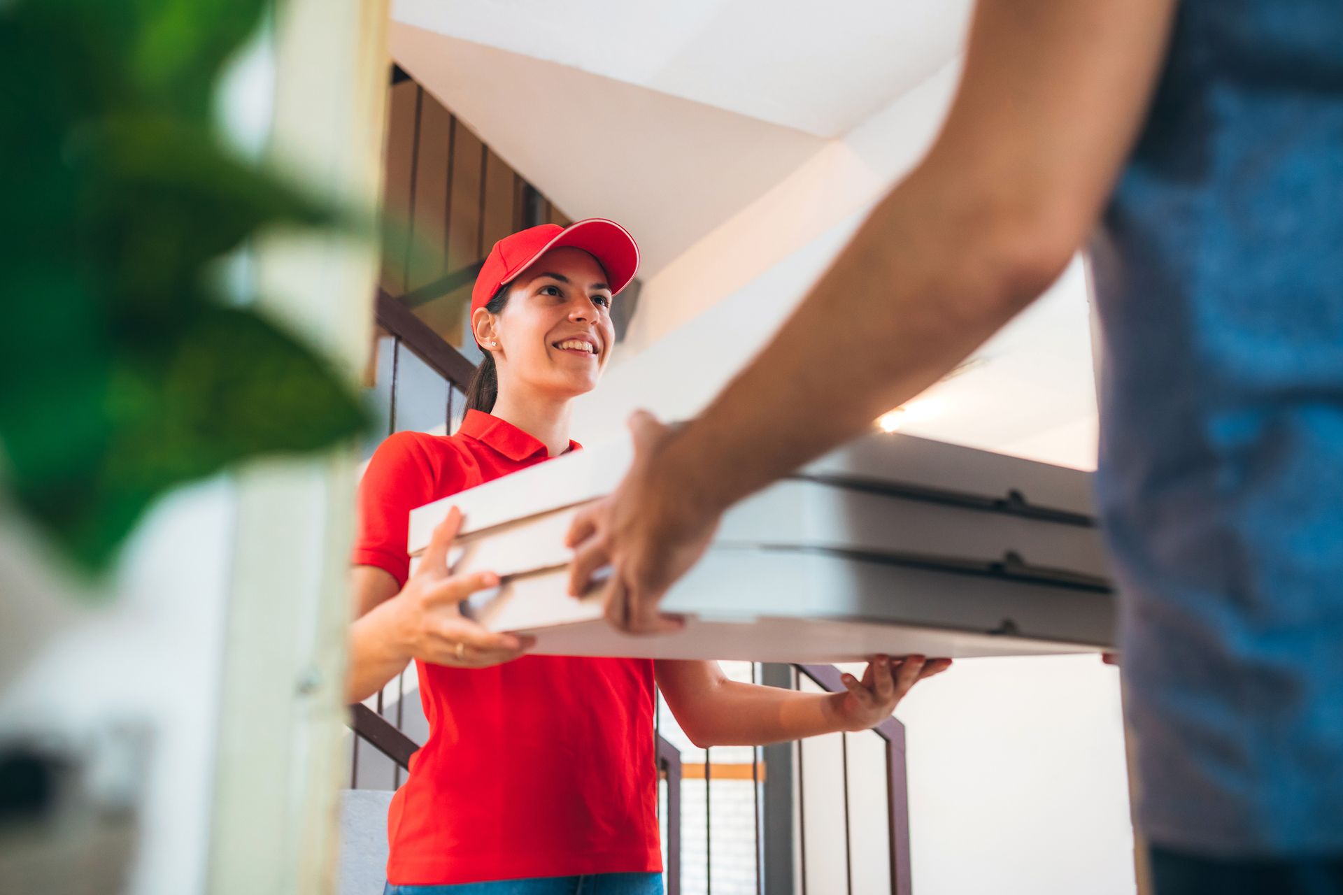 A pizza delivery woman wearing a red cap and t-shirt giving pizza boxes to a customer. A pizza delivery woman wearing a red cap and t-shirt giving pizza boxes to a customer.