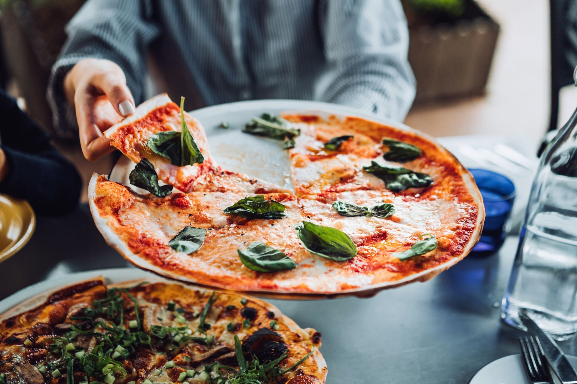 A person holding pizza with fresh basil, highlighting delicious Italian Cuisine & fresh ingredients.