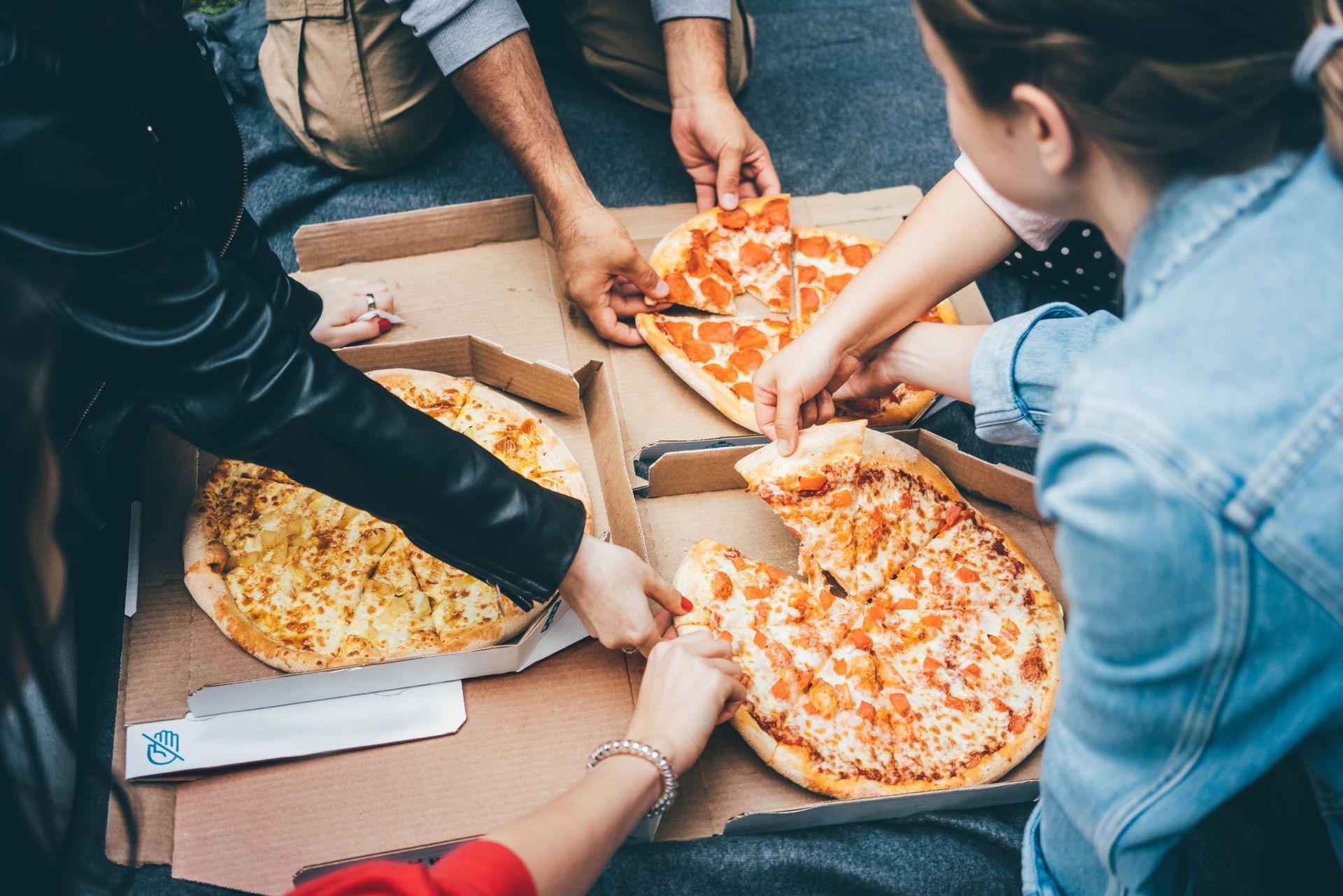 A group of people grabs slices of pizza from a pizza delivery sent by Italian Fiesta Pizzeria in Chi