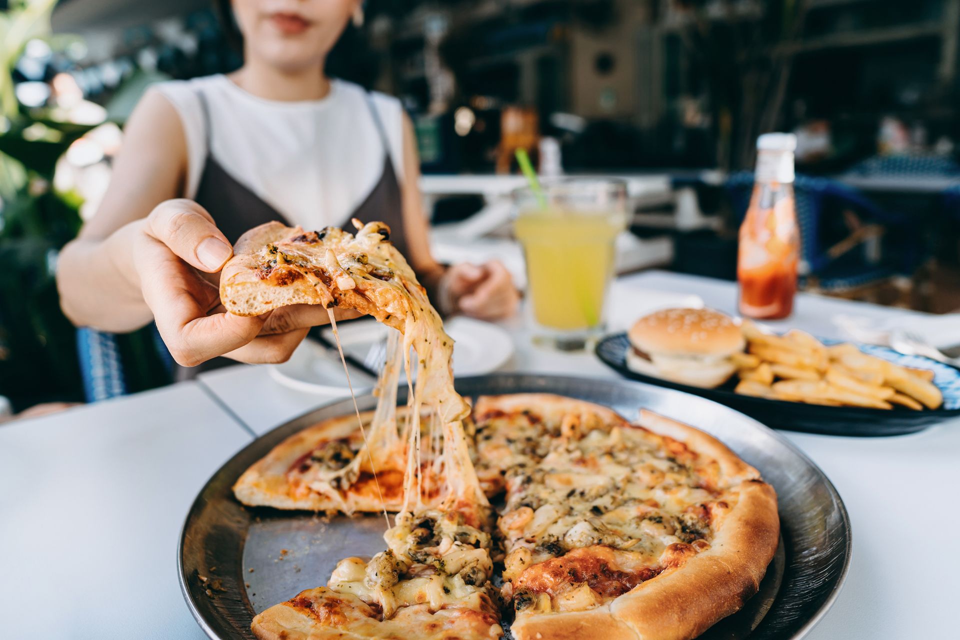 Hand pulling cheesy pizza slice at restaurant table, showcasing Italian cuisine and fresh toppings.