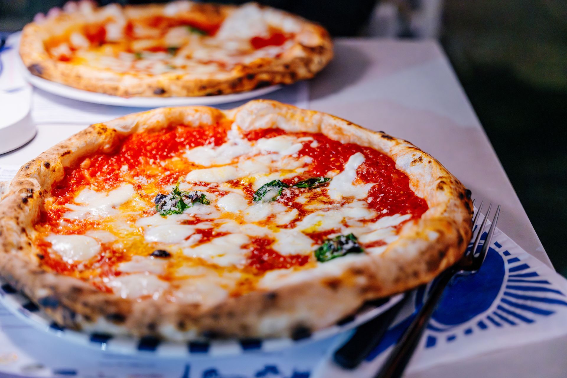 Two pizzas with tomato sauce, mozzarella, and basil on a table.