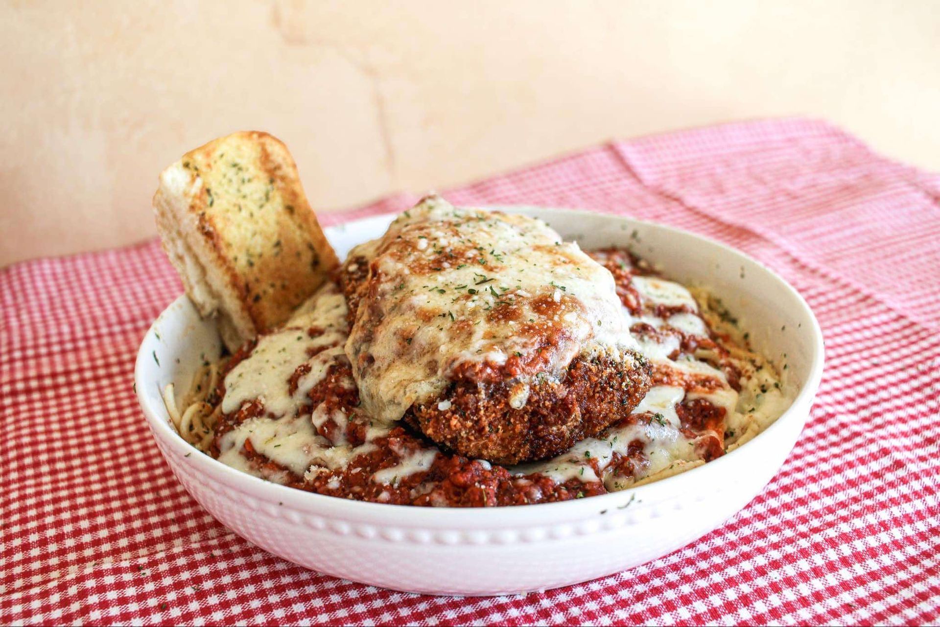 A bowl of spaghetti with meat and cheese and garlic bread on a table.