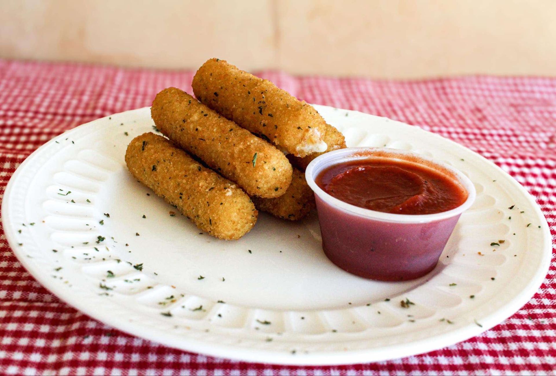 A white plate topped with mozzarella sticks and a cup of ketchup.