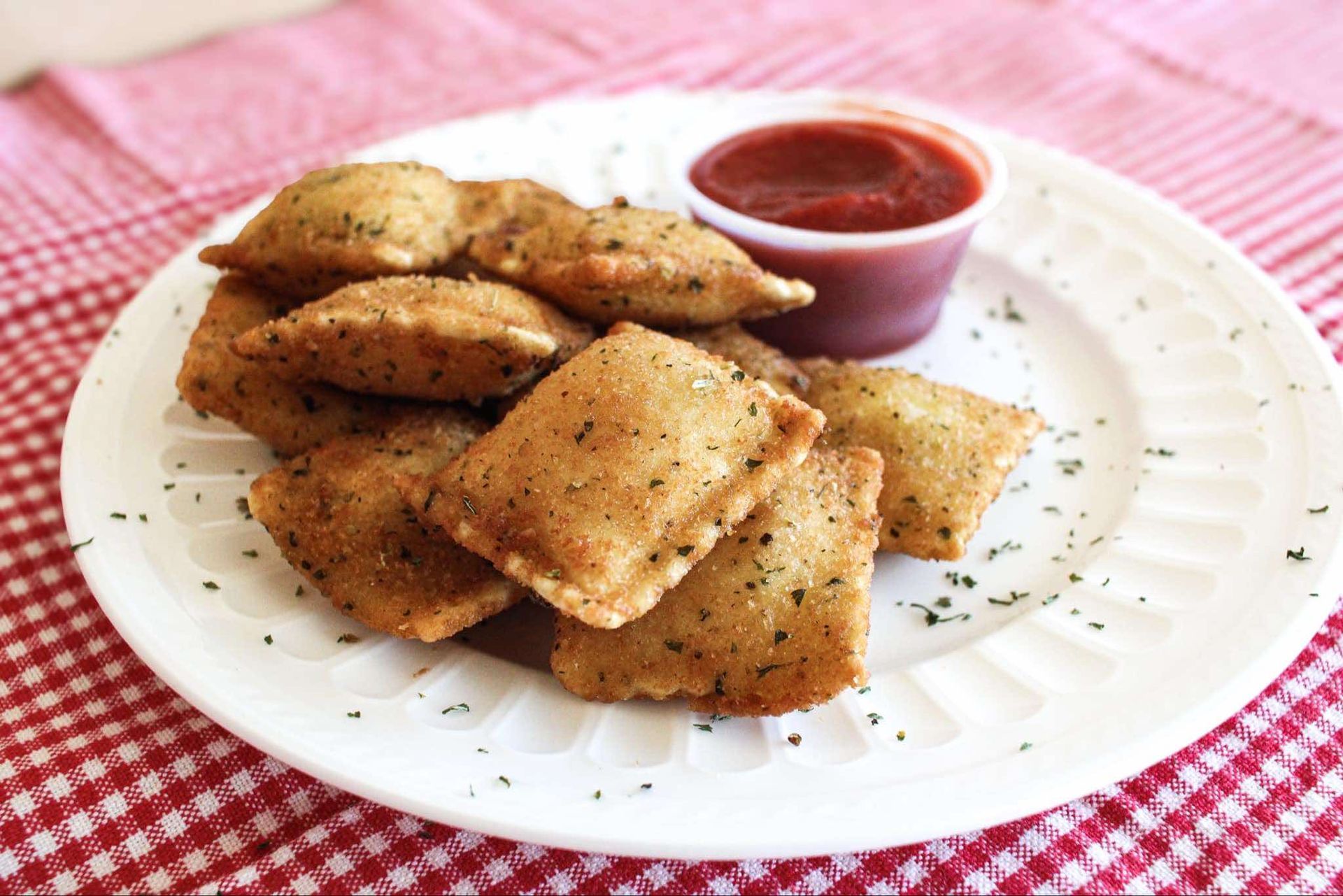 A white plate topped with ravioli next to a cup of ketchup