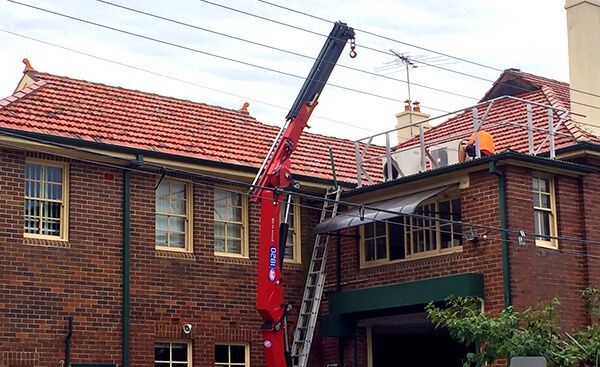 Red crane lifting towards a building with a red tile roof and workers. 