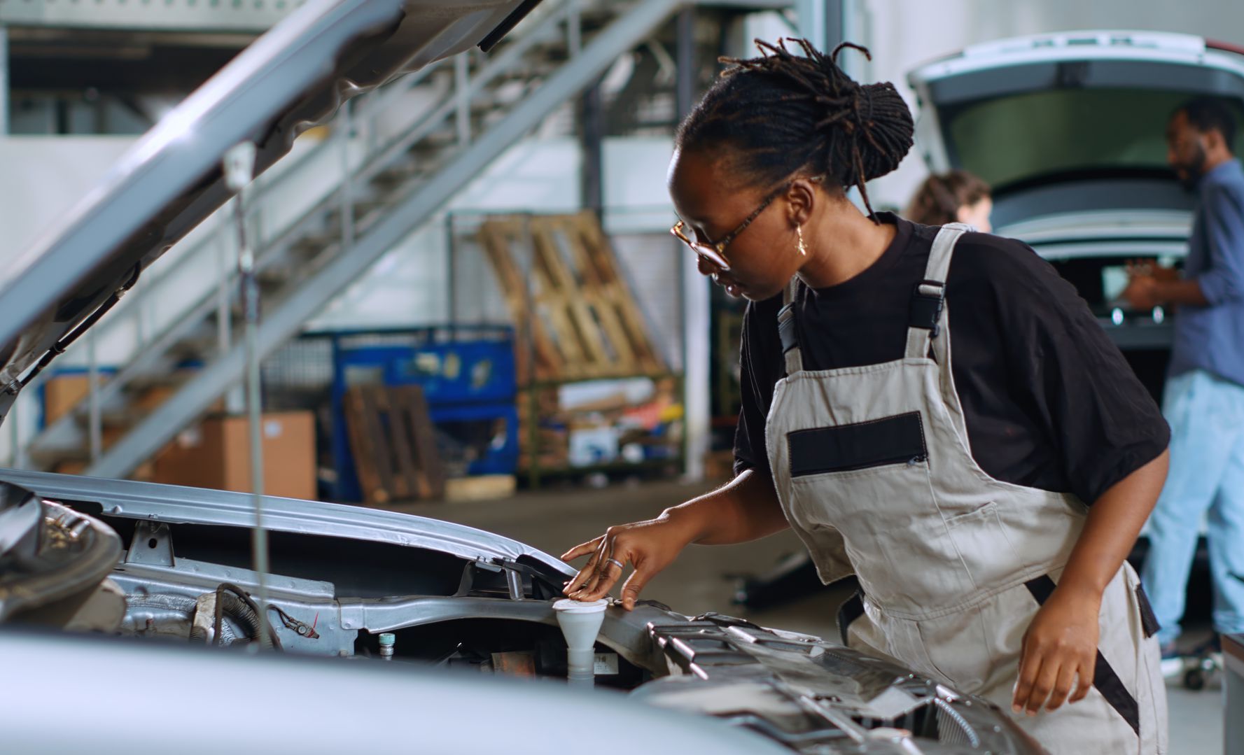 Mechanic in overalls pouring fluid into a car engine at a repair shop.