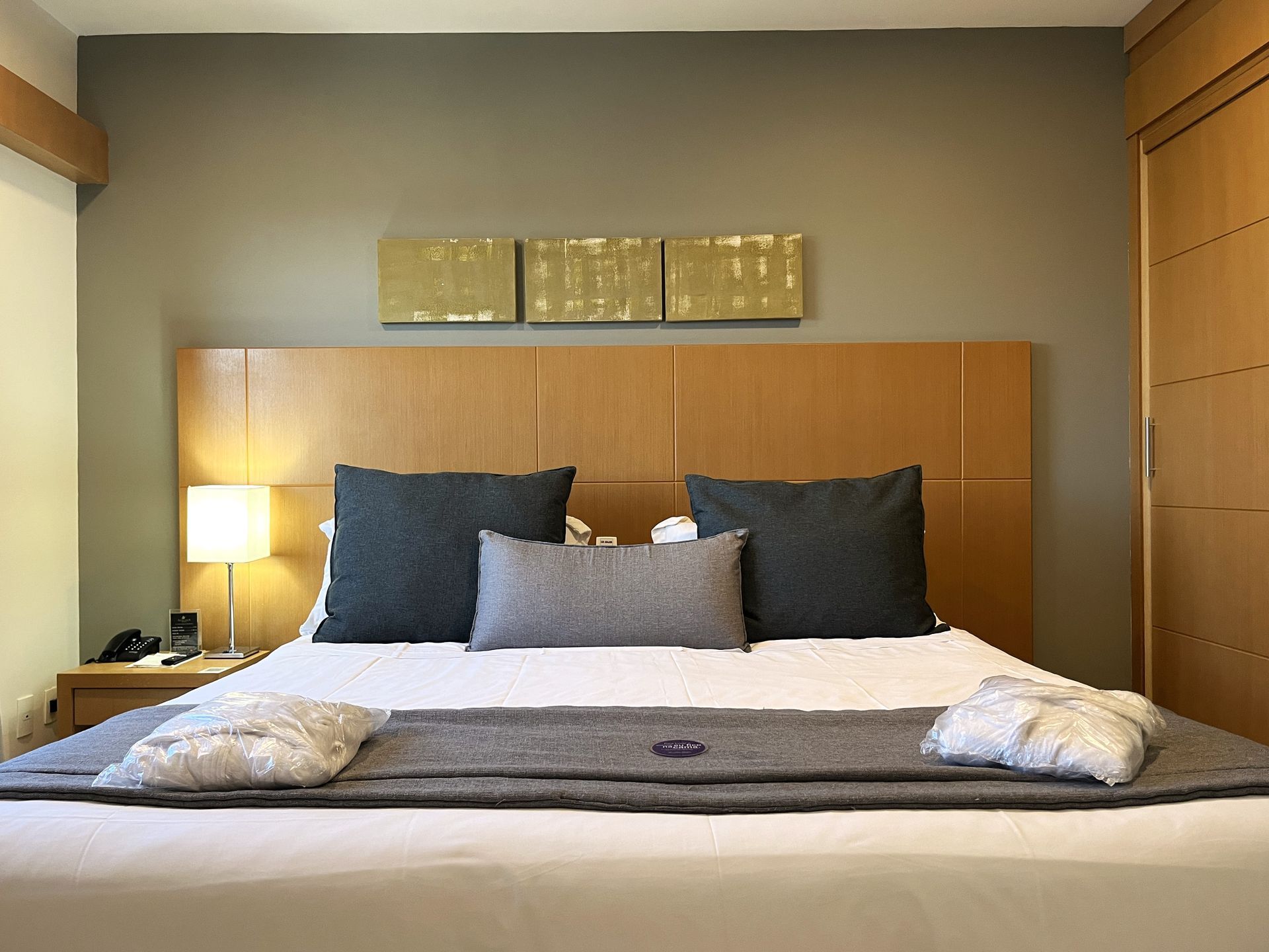 Uma cama king size com roupões sobre a peseira, almofadas e abajur lateral.