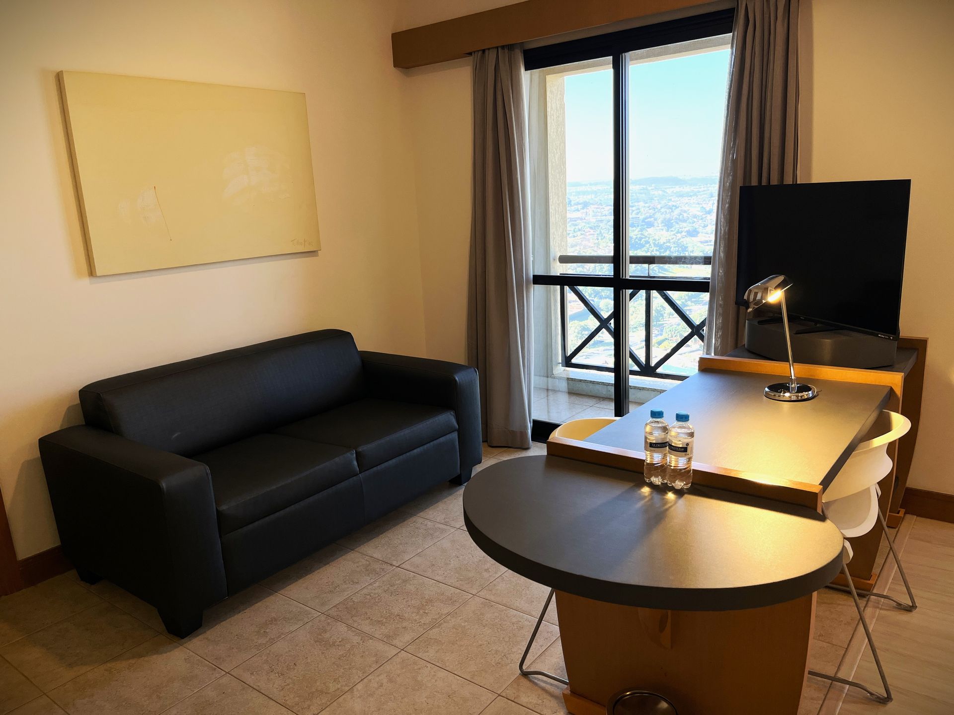 Antessala de quarto de Hotel com sofá e escrivaninha com luminária.