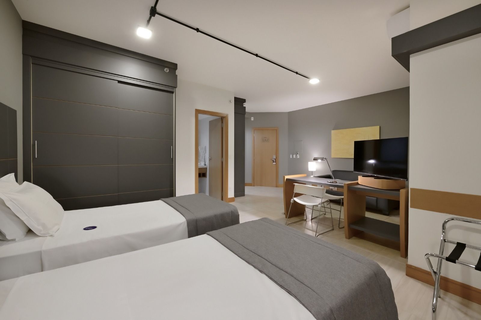 Um quarto de hotel com duas camas de solteiro, uma escrivaninha e uma televisão.