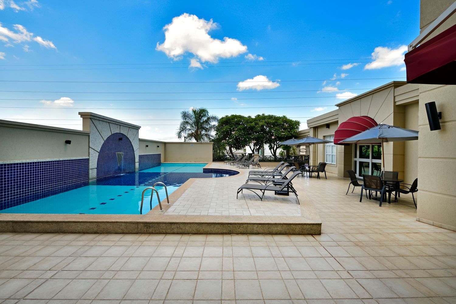 Uma grande piscina com cadeiras e guarda-sóis em frente a um prédio.