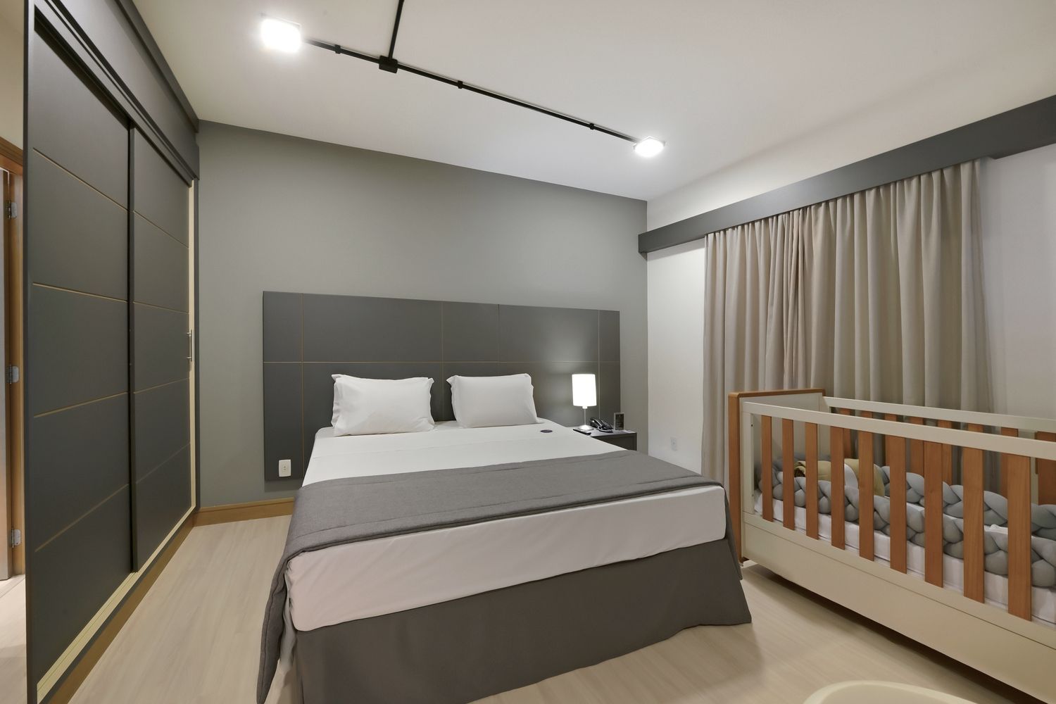 Um quarto de Hotel com uma cama queen size e berço.