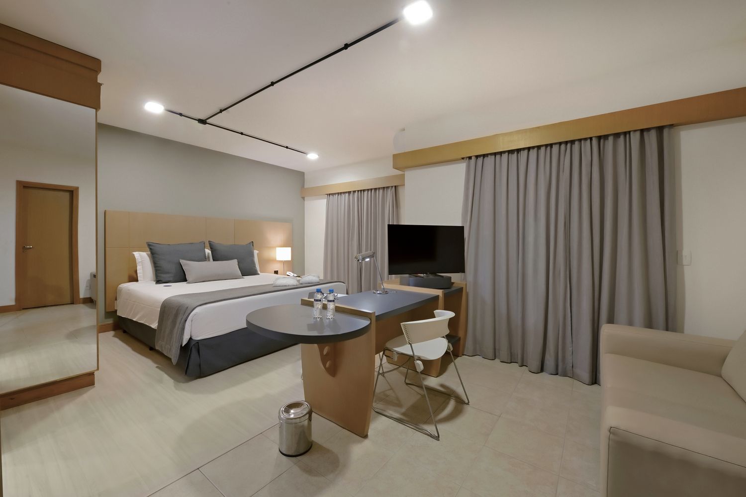 Um quarto de hotel com uma cama king size, escrivaninha, cadeira e televisão.