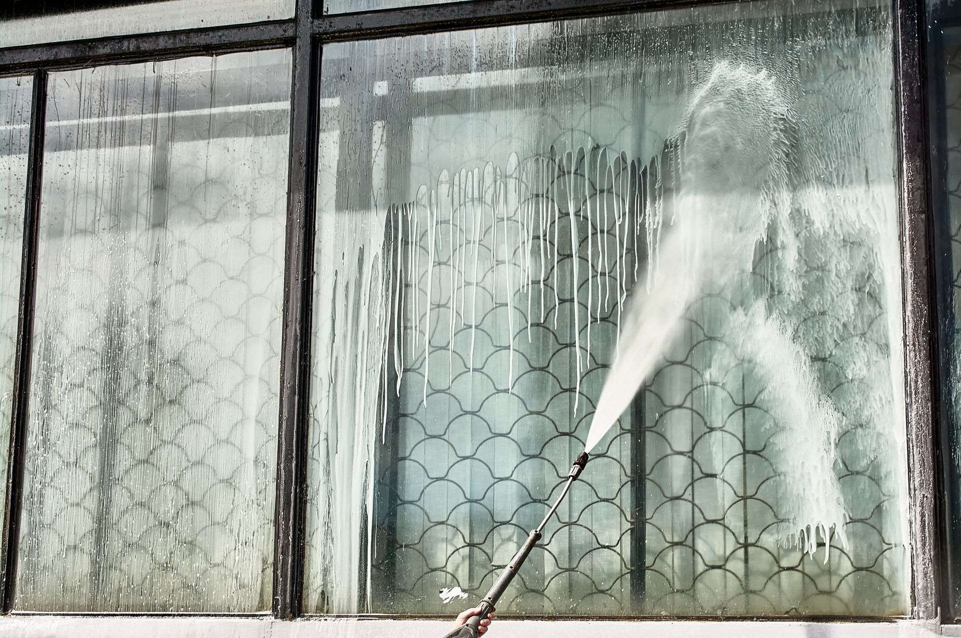 A person is cleaning a window with a high pressure washer.