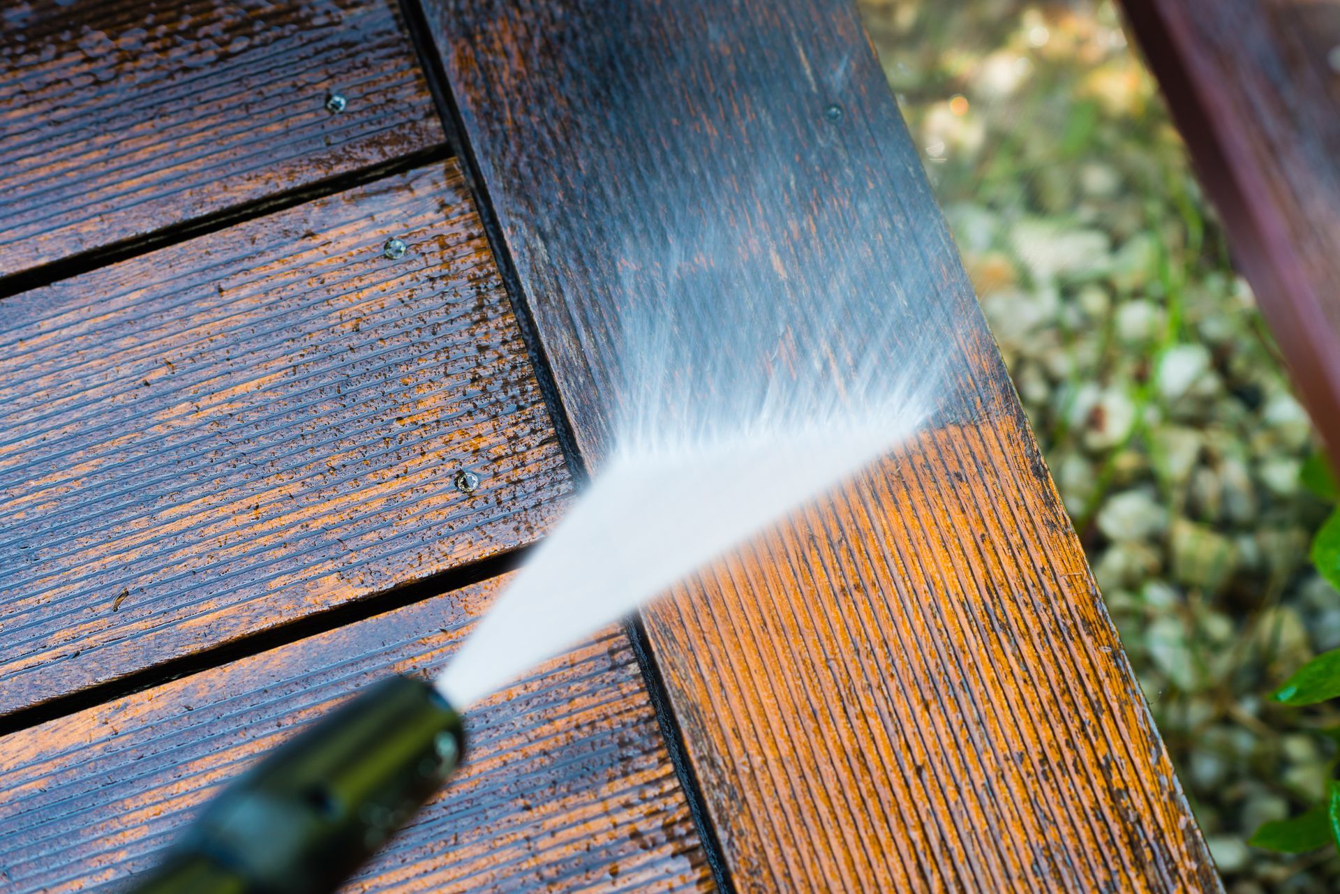 A person is using a high pressure washer to clean a wooden deck.