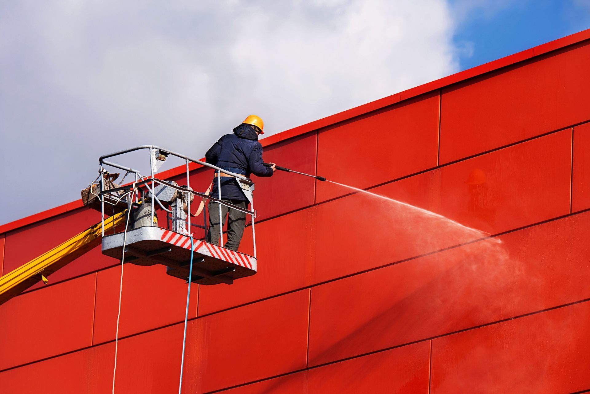 A man is cleaning a red building with a high pressure washer.