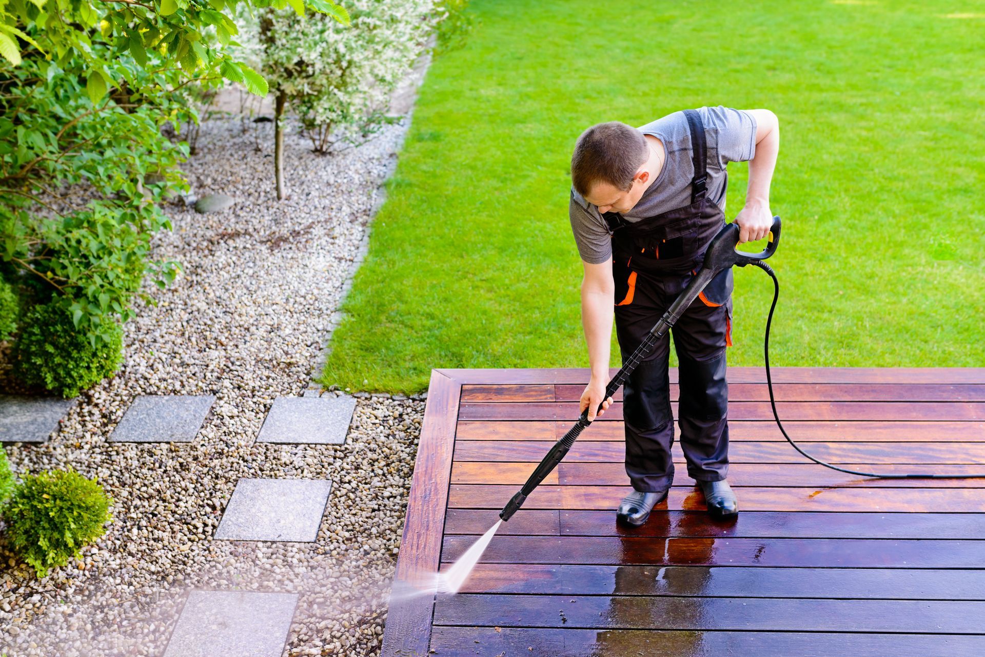 A man is cleaning a wooden deck with a high pressure washer.