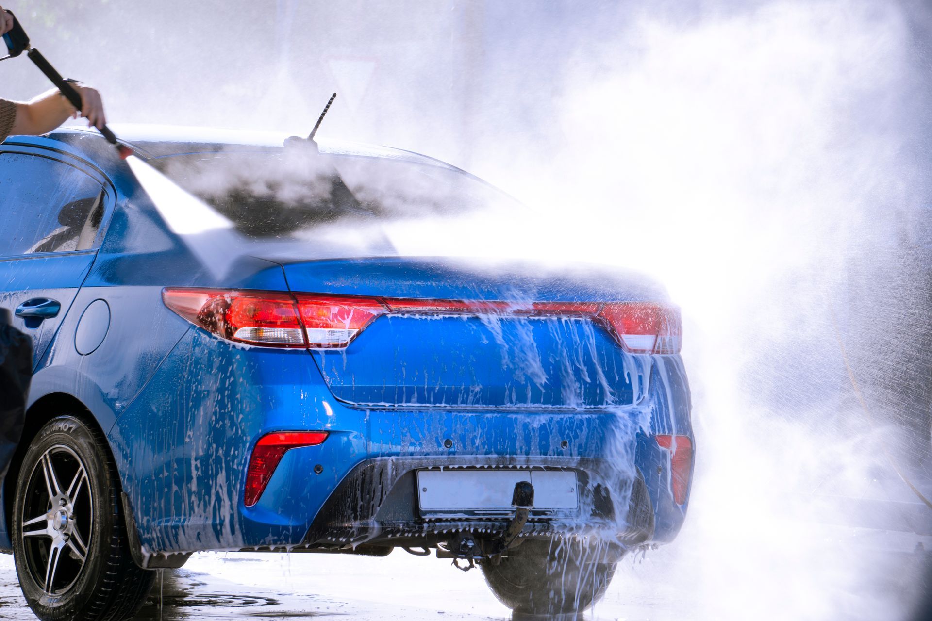 A man is washing a blue car with a high pressure washer.
