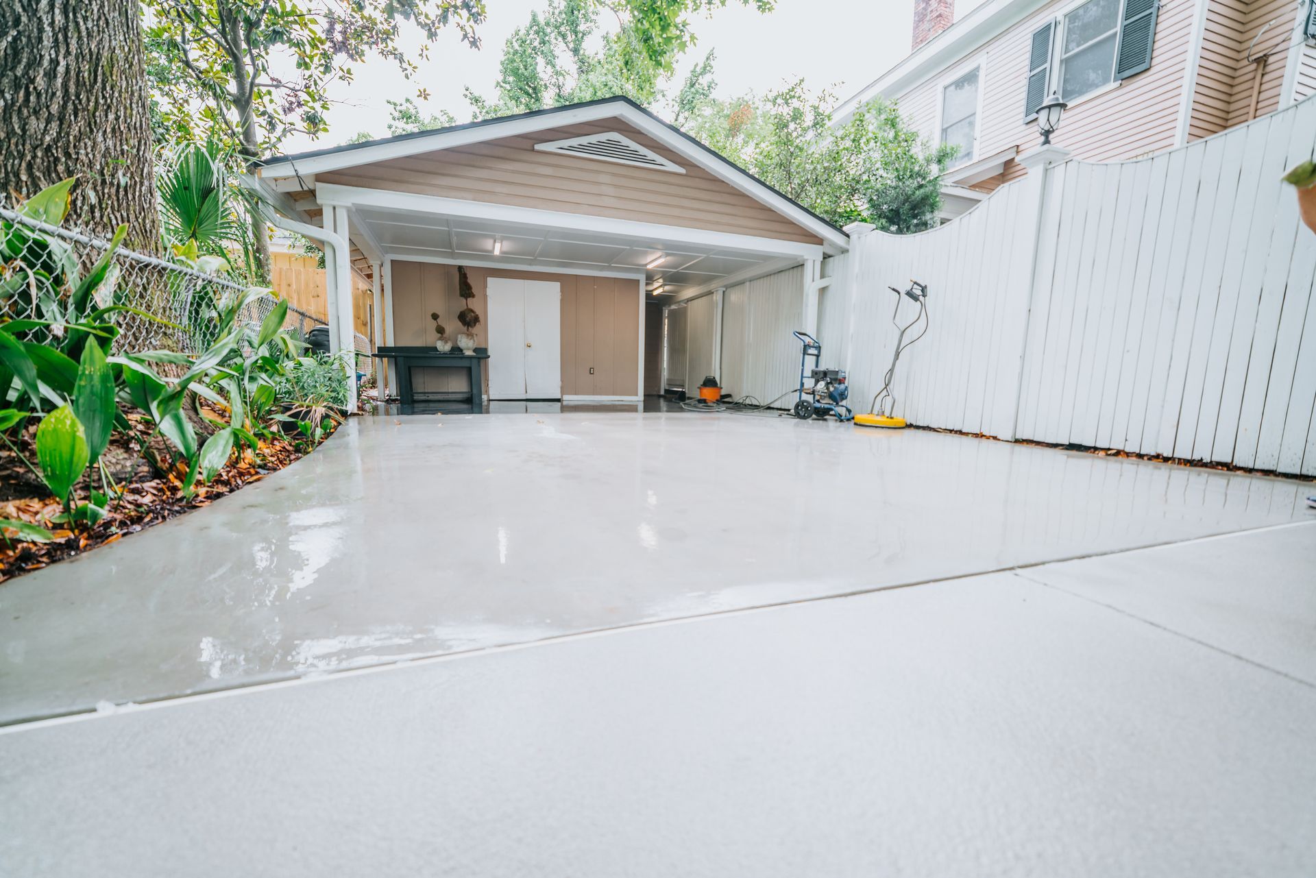 A concrete driveway leading to a garage with a white fence.
