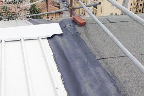 un tetto non ancora ultimato, si vedono travi di ferro una lastra di metallo bianca e un mattone