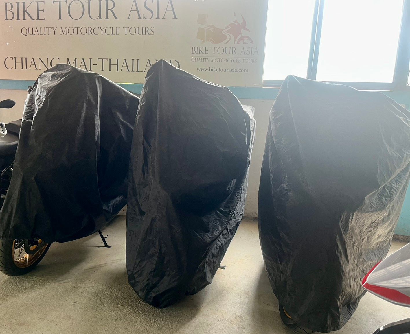 Three motorcycles are covered in black plastic covers in a room.