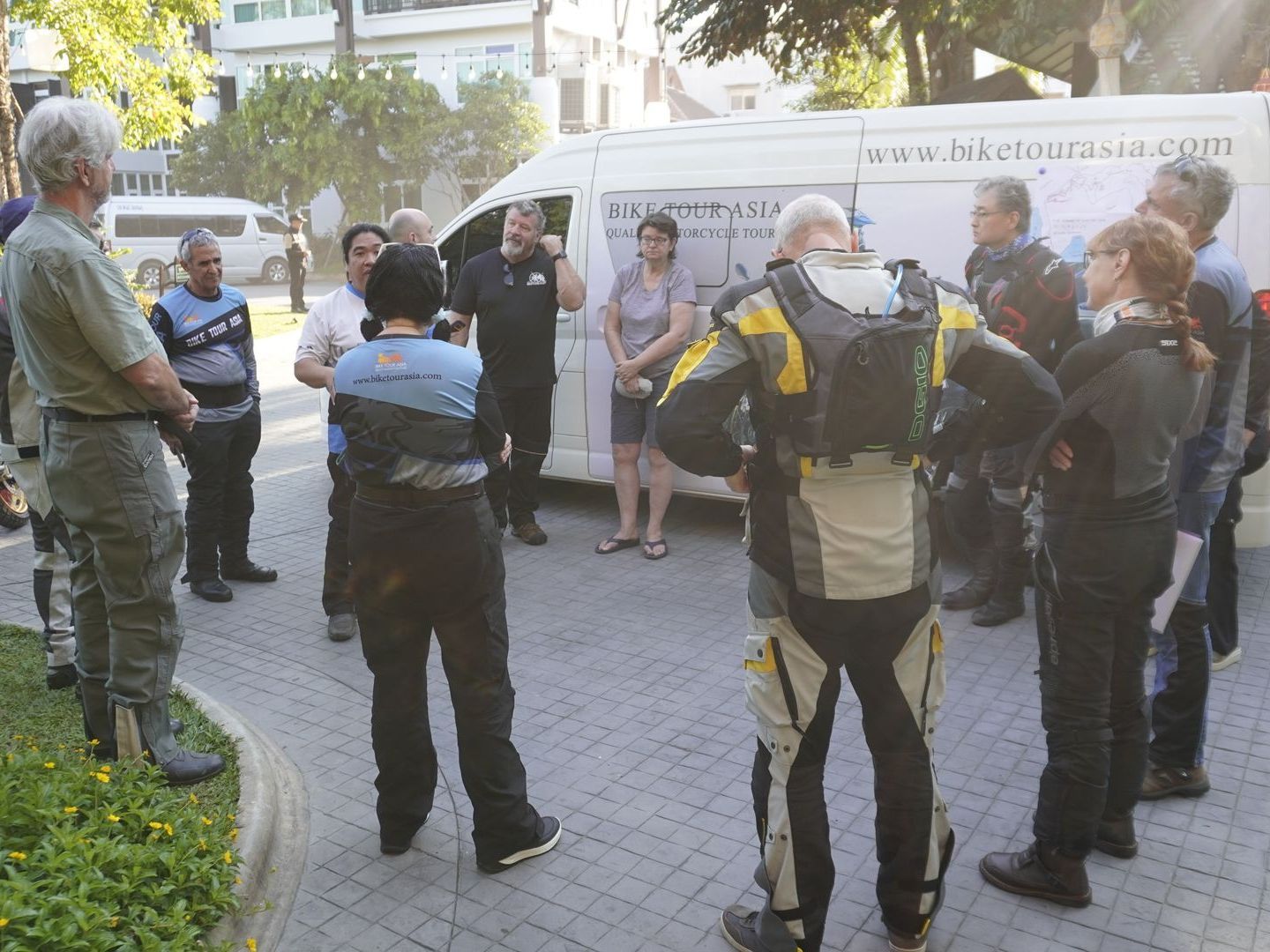 A group of people are standing in front of a white van that says www.hermitage.com