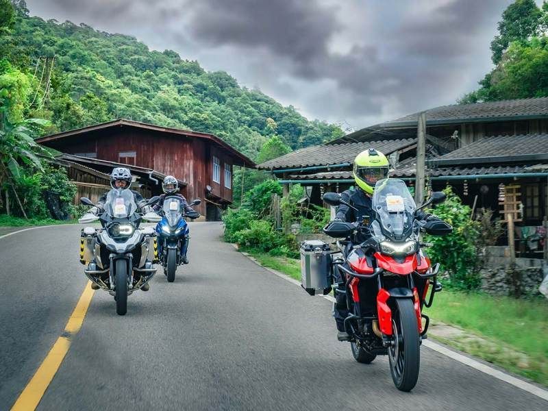 Three Bike Tour Asia riders traveling through a mountain village in northern Thailand on a scenic winding road