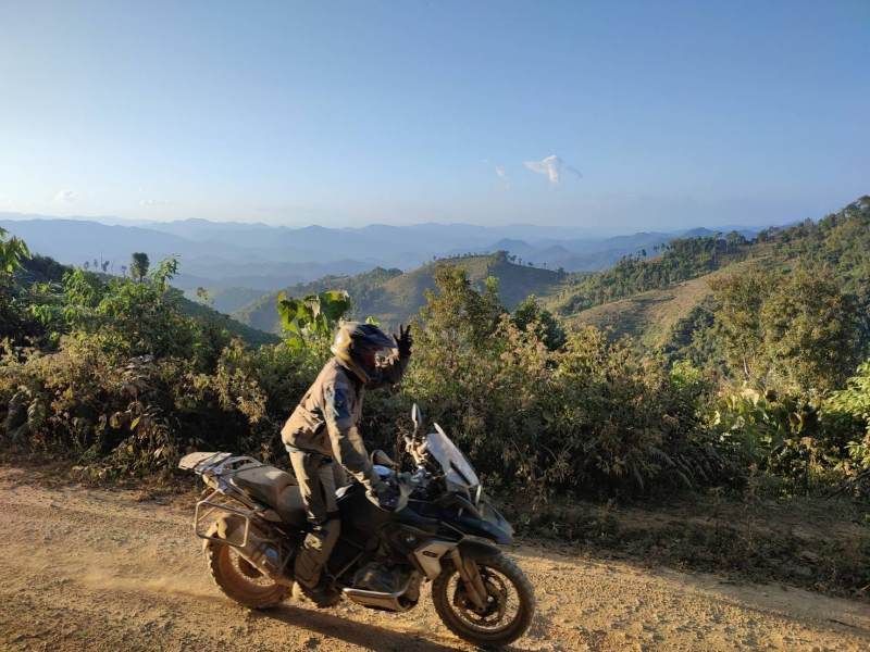 A motorcycle rider on an off-road mountain trail in northern Thailand with sweeping views of layered blue mountain ranges