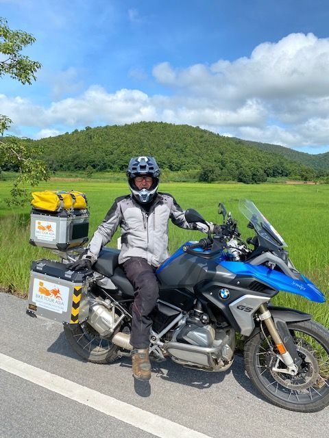 Adventure motorcyclist on a BMW GS touring bike beside green rice fields near Chiang Mai Thailand