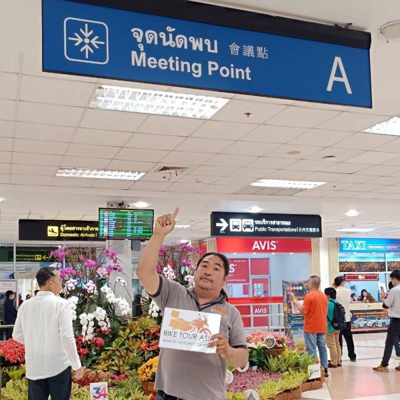 Bike Tour Asia staff holding a welcome sign at the Meeting Point A area inside Chiang Mai International Airport