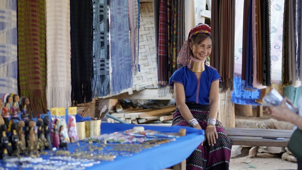 Kayan woman in traditional attire at a cultural village market with handwoven textiles in Northern Thailand