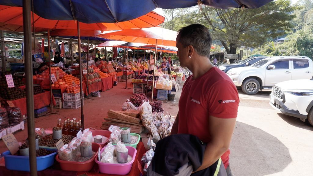 Motorcycle tour rider visiting a local market with fresh produce and spices in Northern Thailand