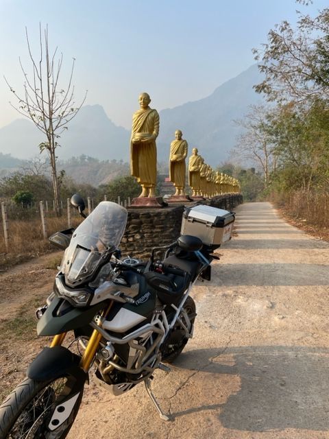 Adventure motorcycle parked beside a line of golden Buddha statues in northern Thailand