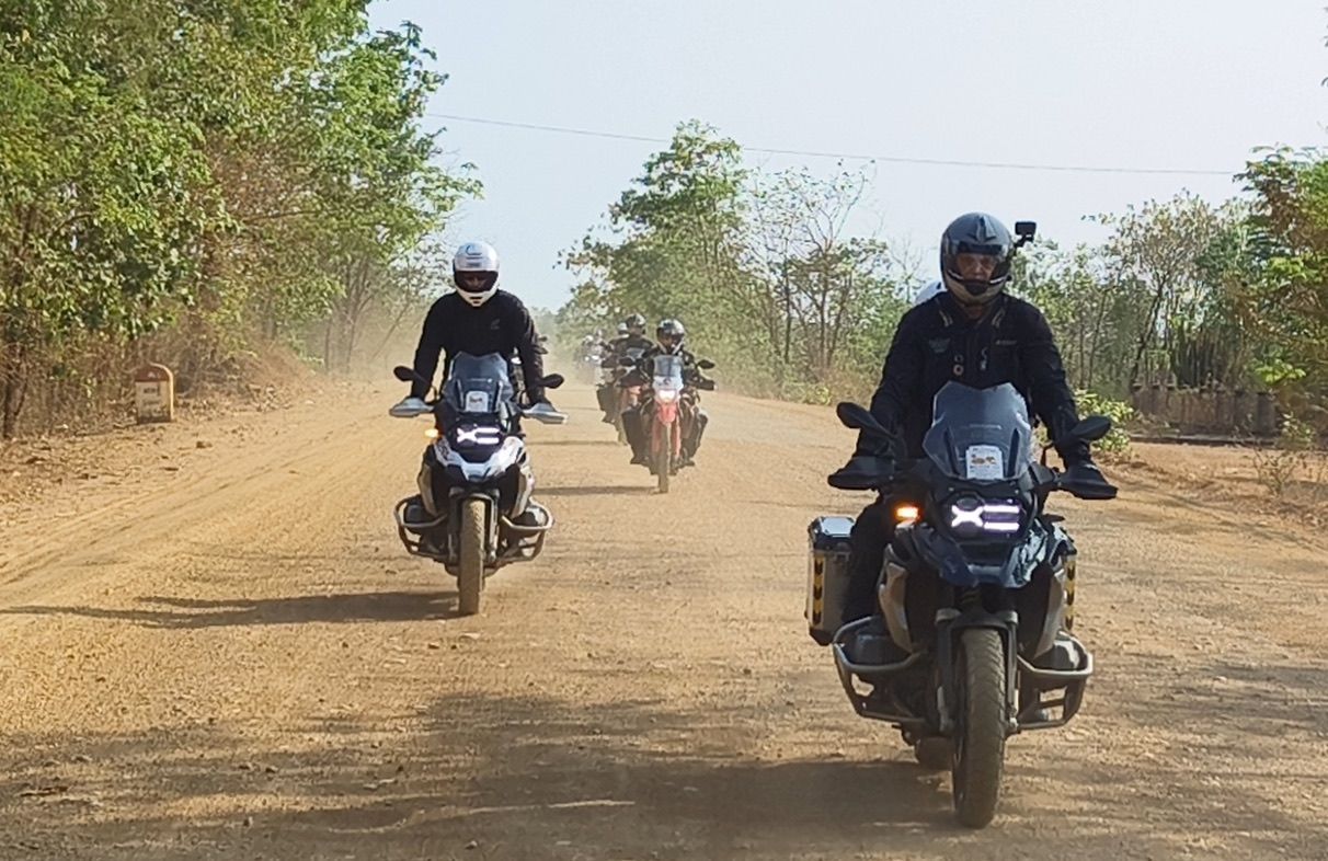 Group of riders on adventure bikes cruising a dusty red road in rural Cambodia
