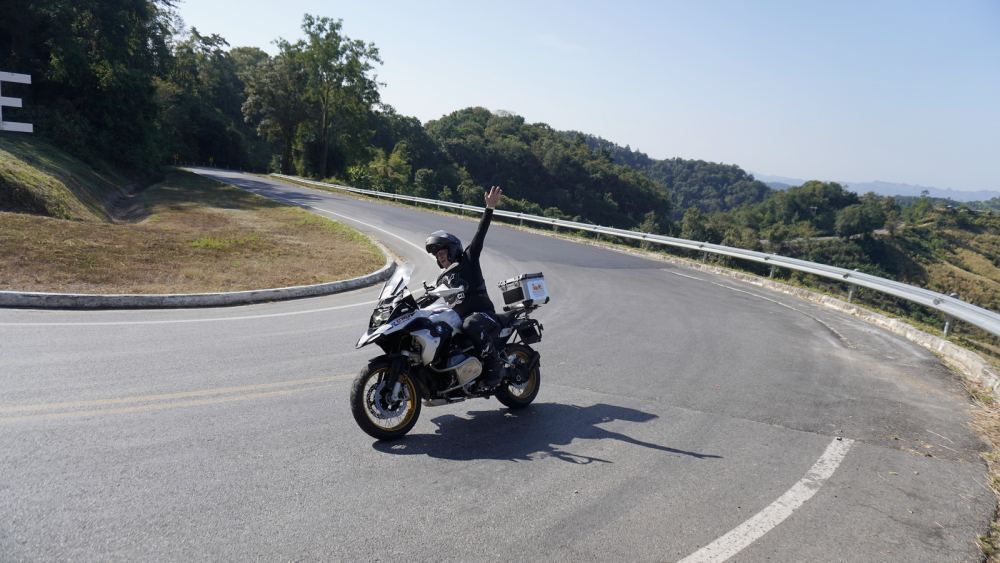 Motorcycle tour rider celebrating on a winding mountain road in Northern Thailand